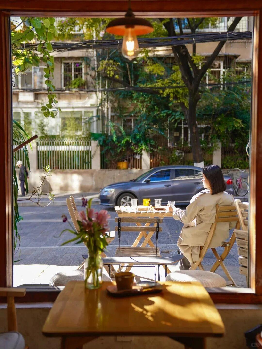 A sunlit café scene viewed through a doorway, with a woman sitting at an outdoor table
